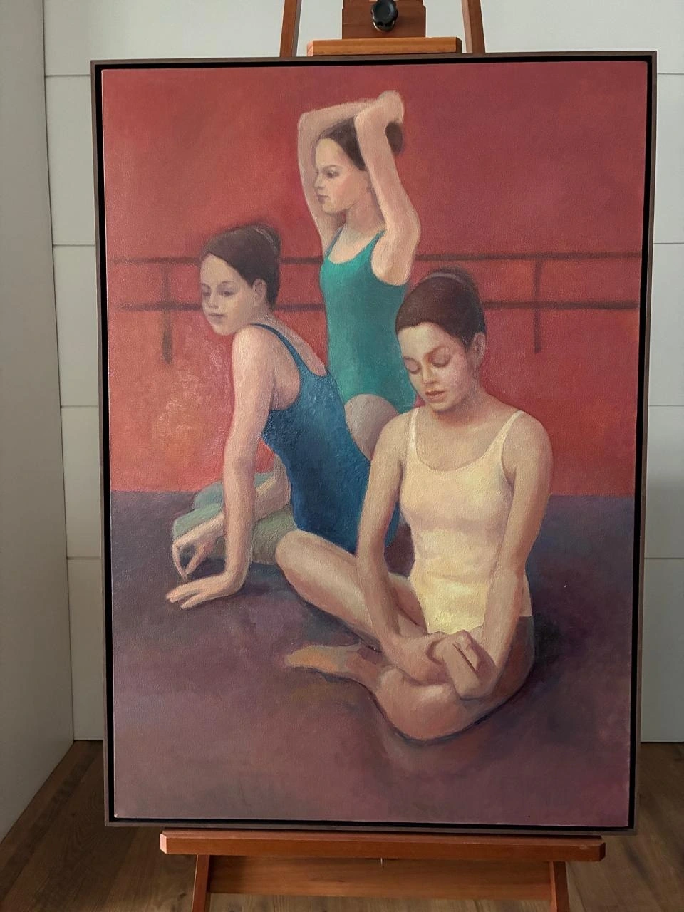 Obra vertical emoldurada com três bailarinas em uma sala de balé, apoiada sobre cavalete